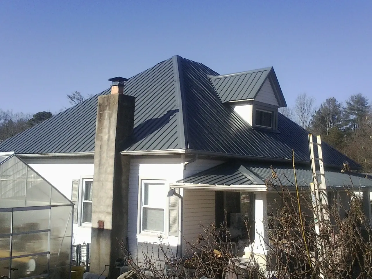 Dark blue standing seam metal roof on a white farmhouse with dormer — Slate & Tile Roof Repair by Roofing Brothers in Cazenovia