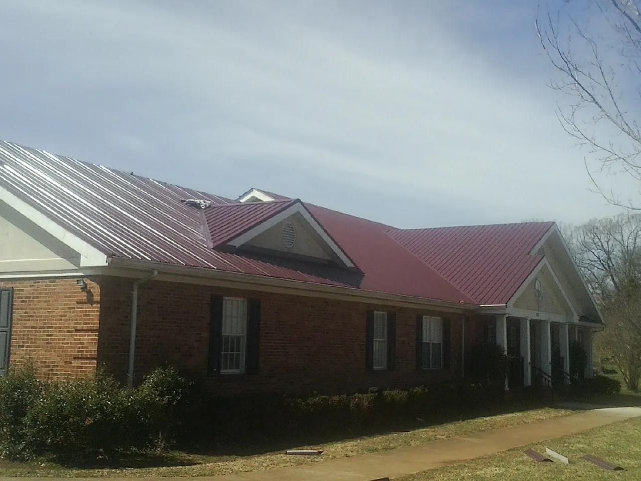 Red metal roof with gabled entries on a long brick building, from a Hail Damage Roof Repair job in Cazenovia