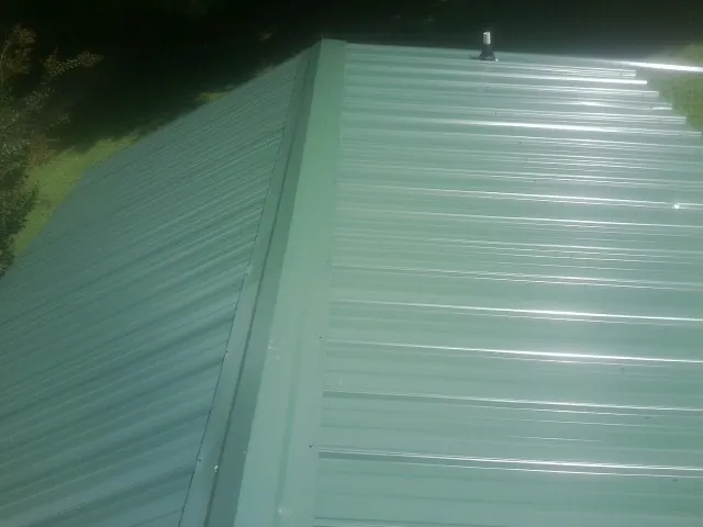 New green metal panels meeting at the ridge of a roof — Flat Roof Repair work by our crew in Cazenovia