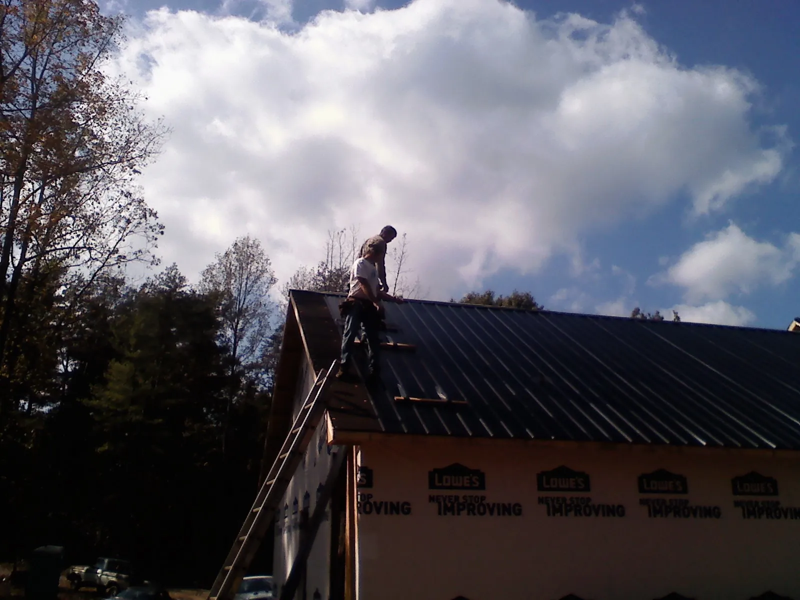 Roofer fastening dark metal panels high against a cloudy sky, from a Roof Inspection job in Cazenovia