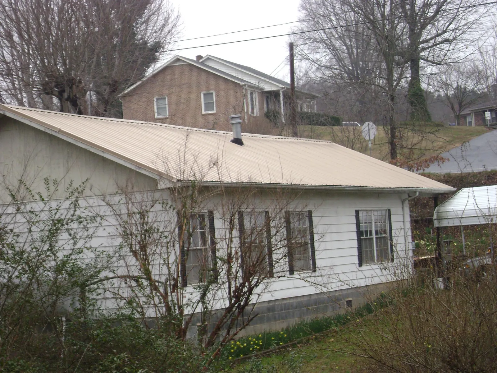 Tan metal roof on a white sided house set into a hillside — Commercial Roofing by Roofing Brothers in Cazenovia