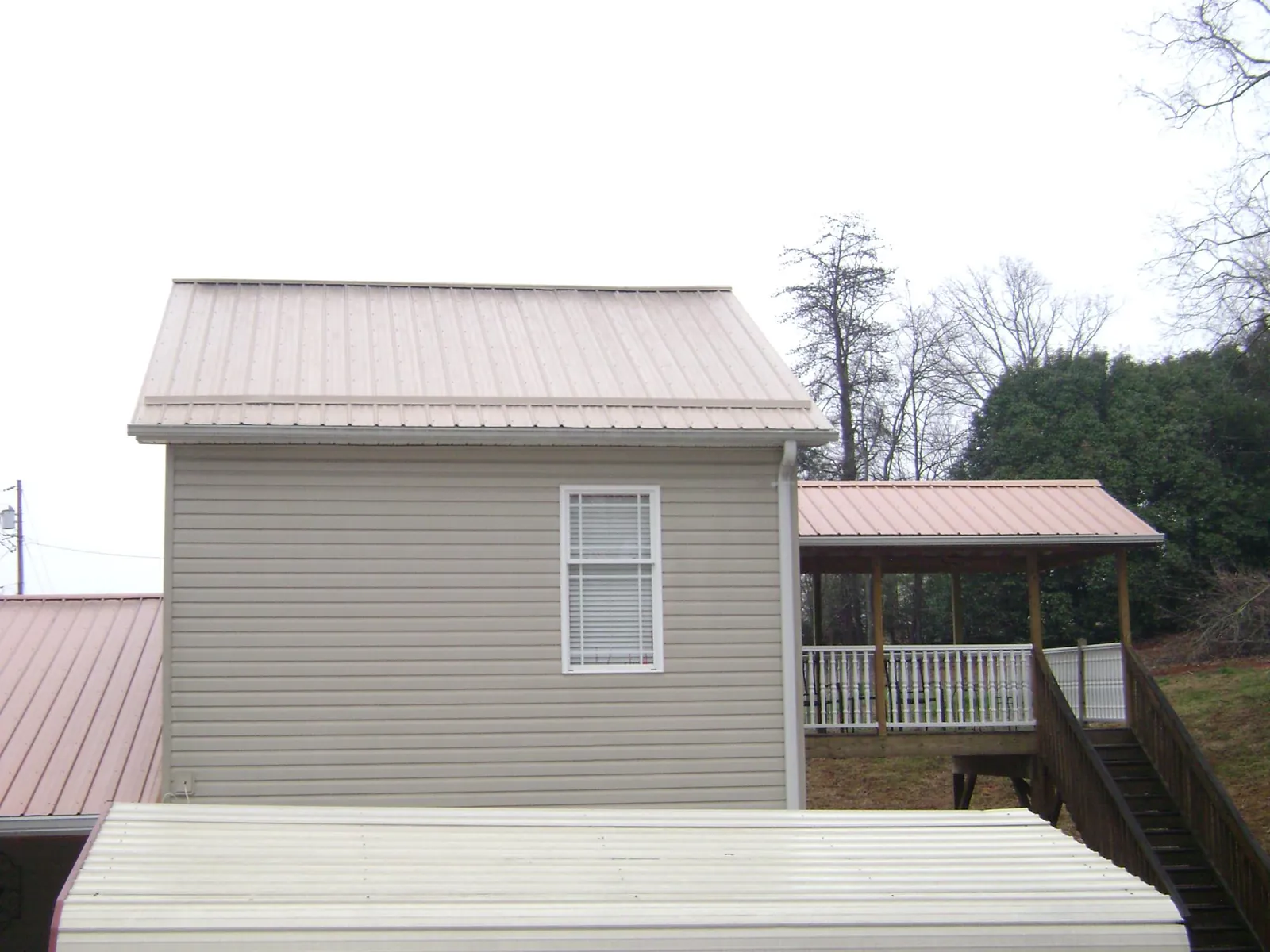 Tan metal roofs on a two story addition and attached porch, from a Roof Replacement job in Cazenovia